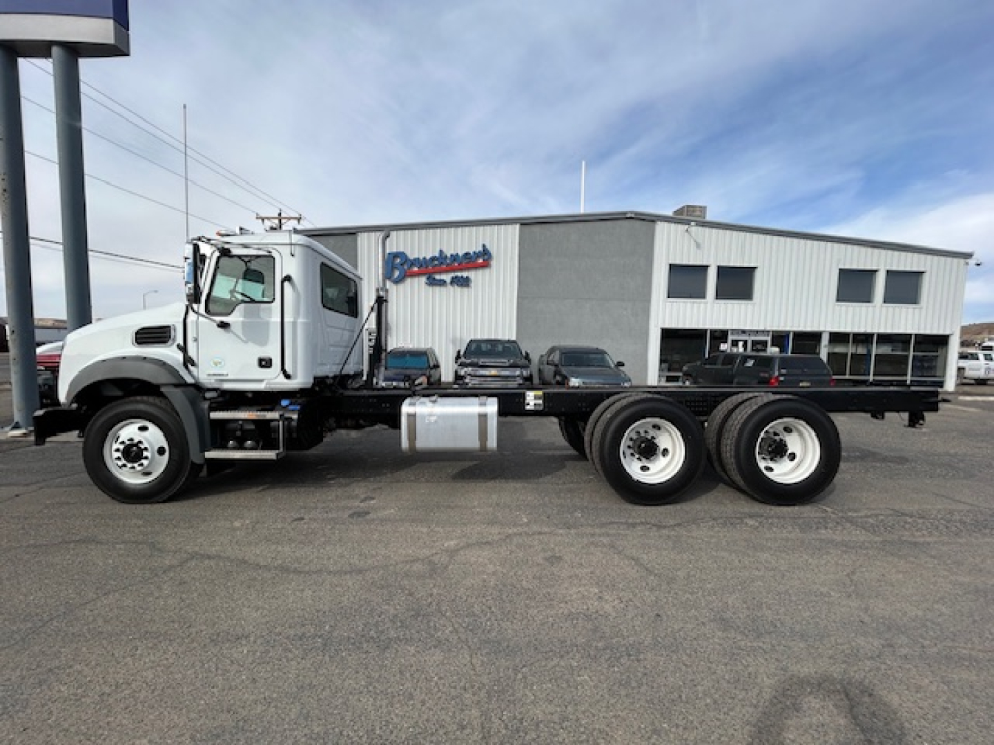 Mack GR64B chassis cab with dual rear axles and white cab, parked in lot in front of dealership building.