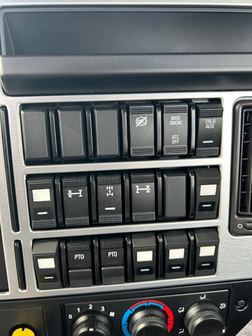 Dashboard switches and controls of a Mack truck cab, including multiple rocker switches with symbols and labels such as PTO, ATC OFF, MUD SNOW, TRLR AUX, and other blank/slotted switches.