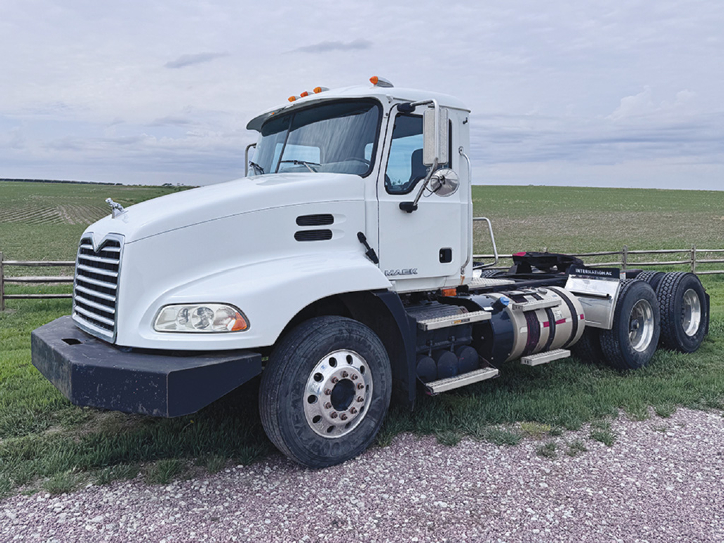 Truck deck space showing 2013 Mack CXU613 conventional daycab, white cab, dual rear axles, stock number 551212, side view.