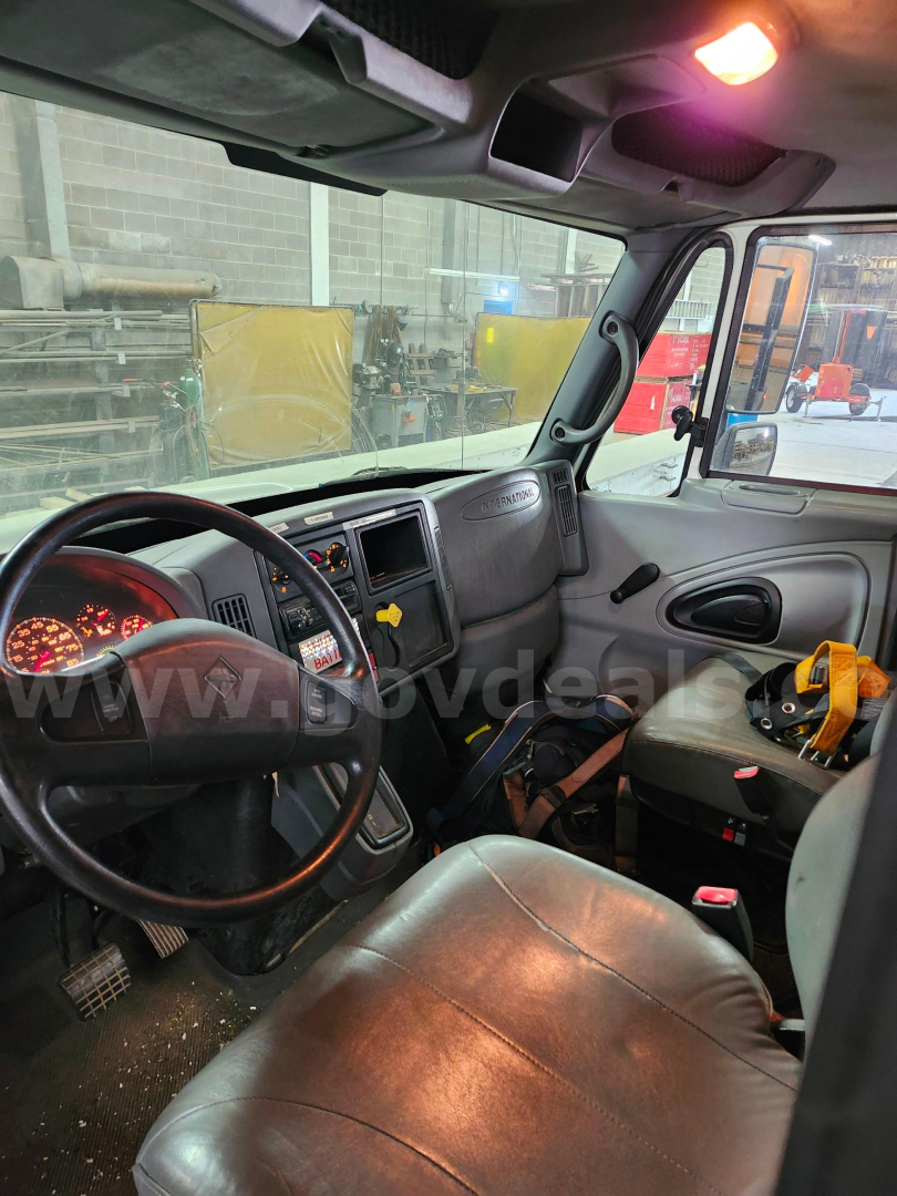 Truck cab interior of a 2004 International 4200 showing steering wheel, dashboard, and driver seat with visible wear and a yellow tool in the passenger area.