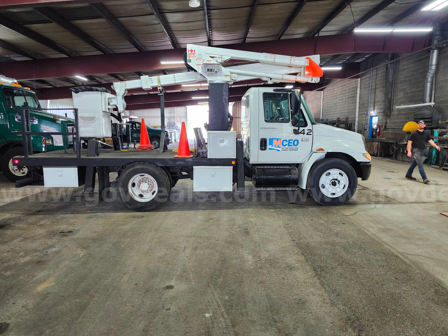 Truck chassis with bucket lift arm extended, International 4200 model, interior cab shows 42 on door, utility markings, inside warehouse.