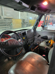 Truck cab interior of a 2004 International 4200 showing steering wheel, dashboard, and driver seat with visible wear and a yellow tool in the passenger area.