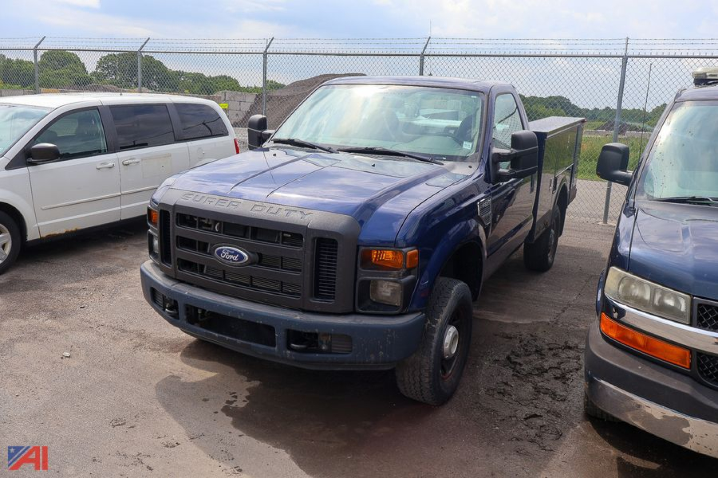 Blue 2008 Ford F-350 Super Duty utility truck parked in a lot with a chain-link fence; front grille shows Ford emblem and 'SUPER DUTY' lettering; other vans nearby.