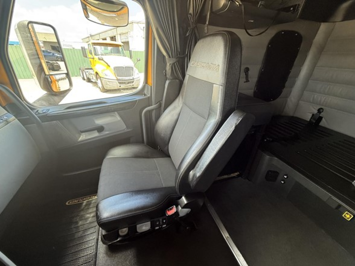 Cabin interior of a Freightliner Cascadia 126 showing a driver's seat, steering area, and sleeper bunk with storage compartments.