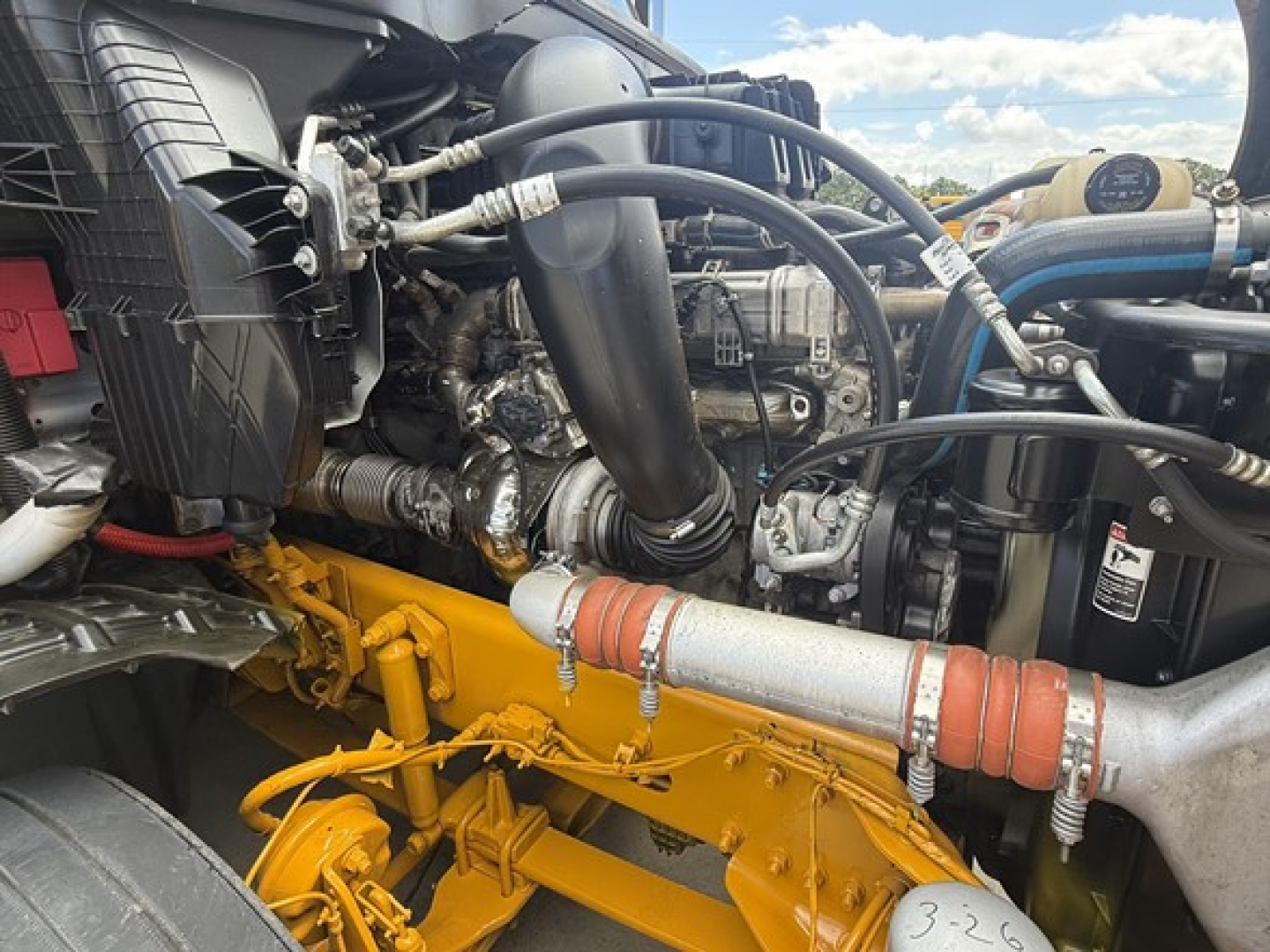 Engine bay of a Freightliner Cascadia 126 showing yellow engine components, hoses, and radiator area with various tubes and clamps visible.