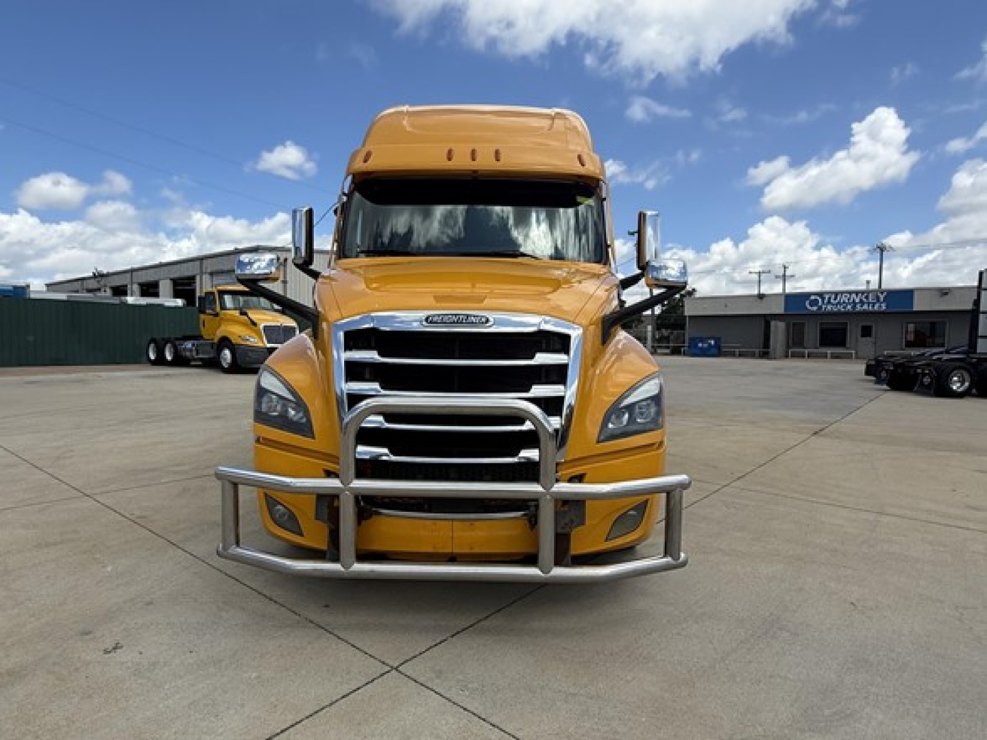Freightliner Cascadia 126 front view showing chrome grille, bumper guard, and yellow cab in a dealership lot.