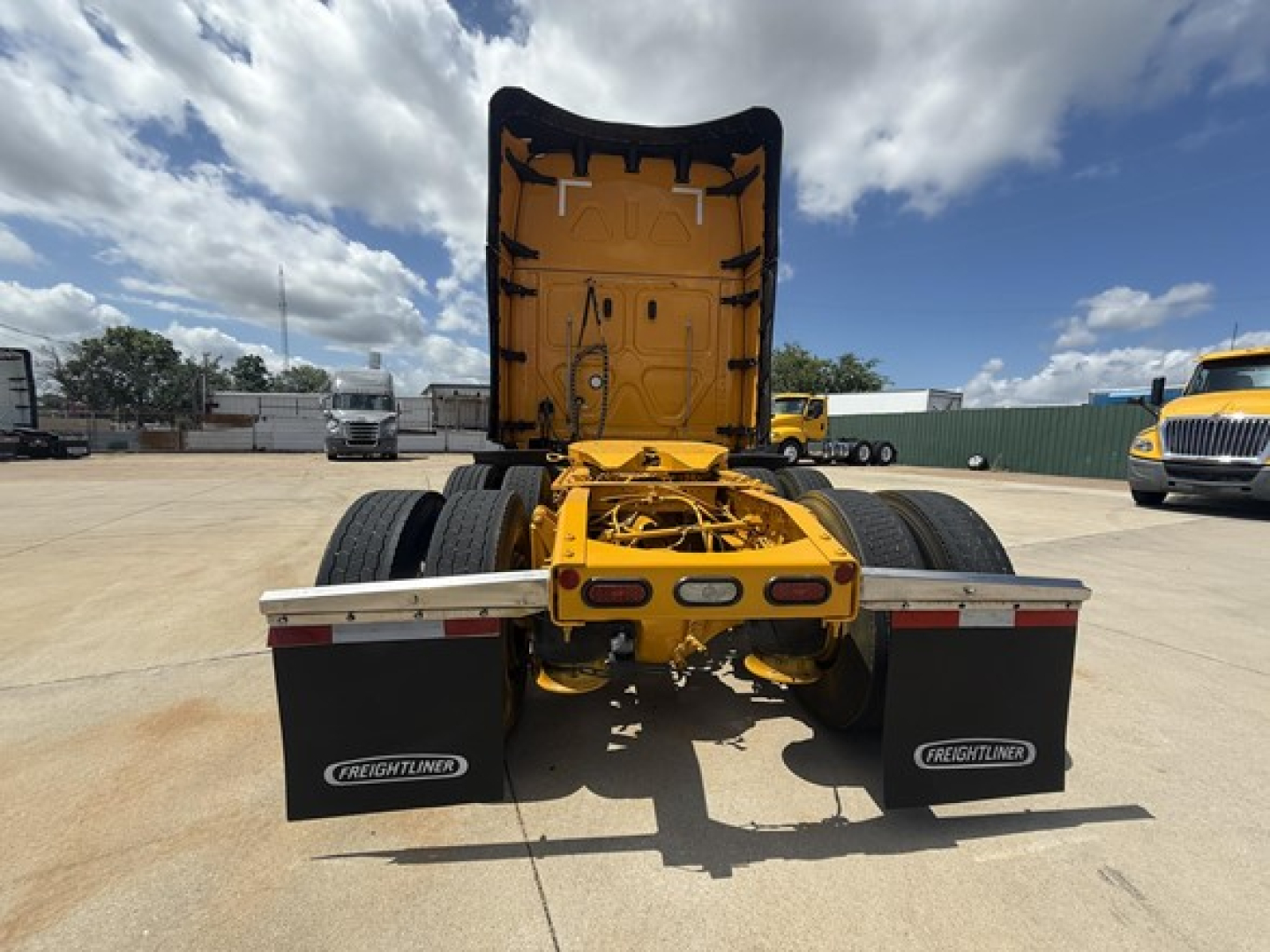 Yellow Freightliner Cascadia 126 tractor rear with mudflaps showing Freightliner logo, open sleeper cab back, chassis, dual rear axles.