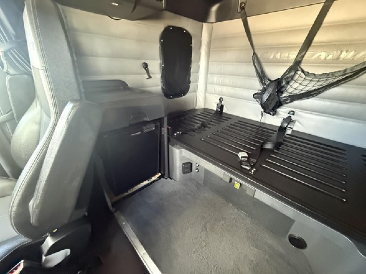Freightliner Cascadia 126 sleeper cab interior showing side console and cargo bed area with netting and storage shelf.
