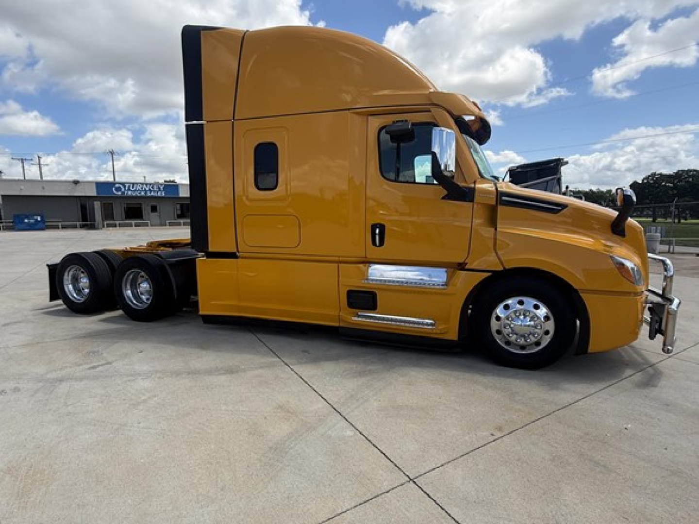 Freightliner Cascadia 126 sleeper tractor in yellow side view showing two rear axles, chrome mirrors, and aerodynamic cab with black accents.