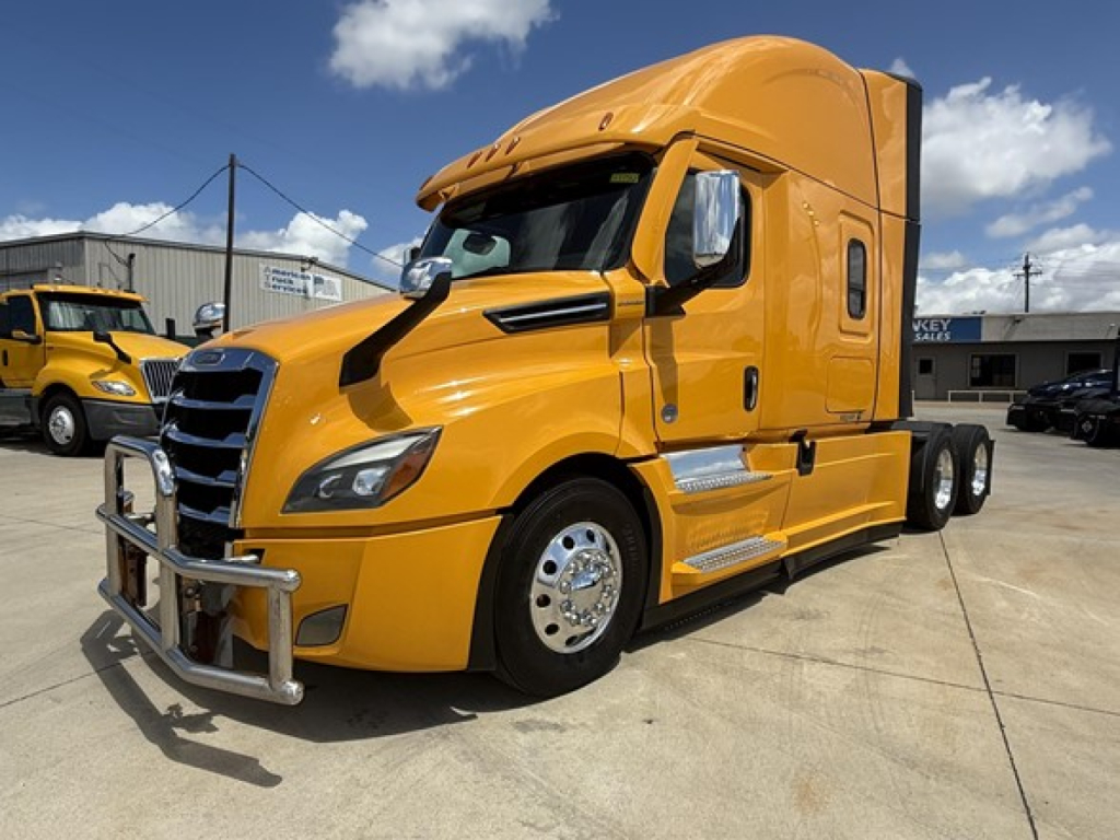 Freightliner Cascadia 126 sleeper cab in orange, front three-quarter view showing chrome bumper guard, grille, and side steps.