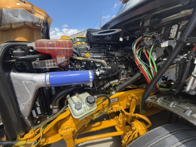 Freightliner Cascadia 126 engine bay showing coolant reservoir, blue silicone hose, multiple wiring harnesses, and yellow factory-painted chassis components.