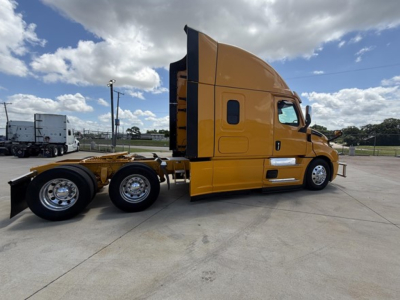 Freightliner Cascadia 126 tractor in yellow/orange color, side view showing sleeper cab and rear axles.