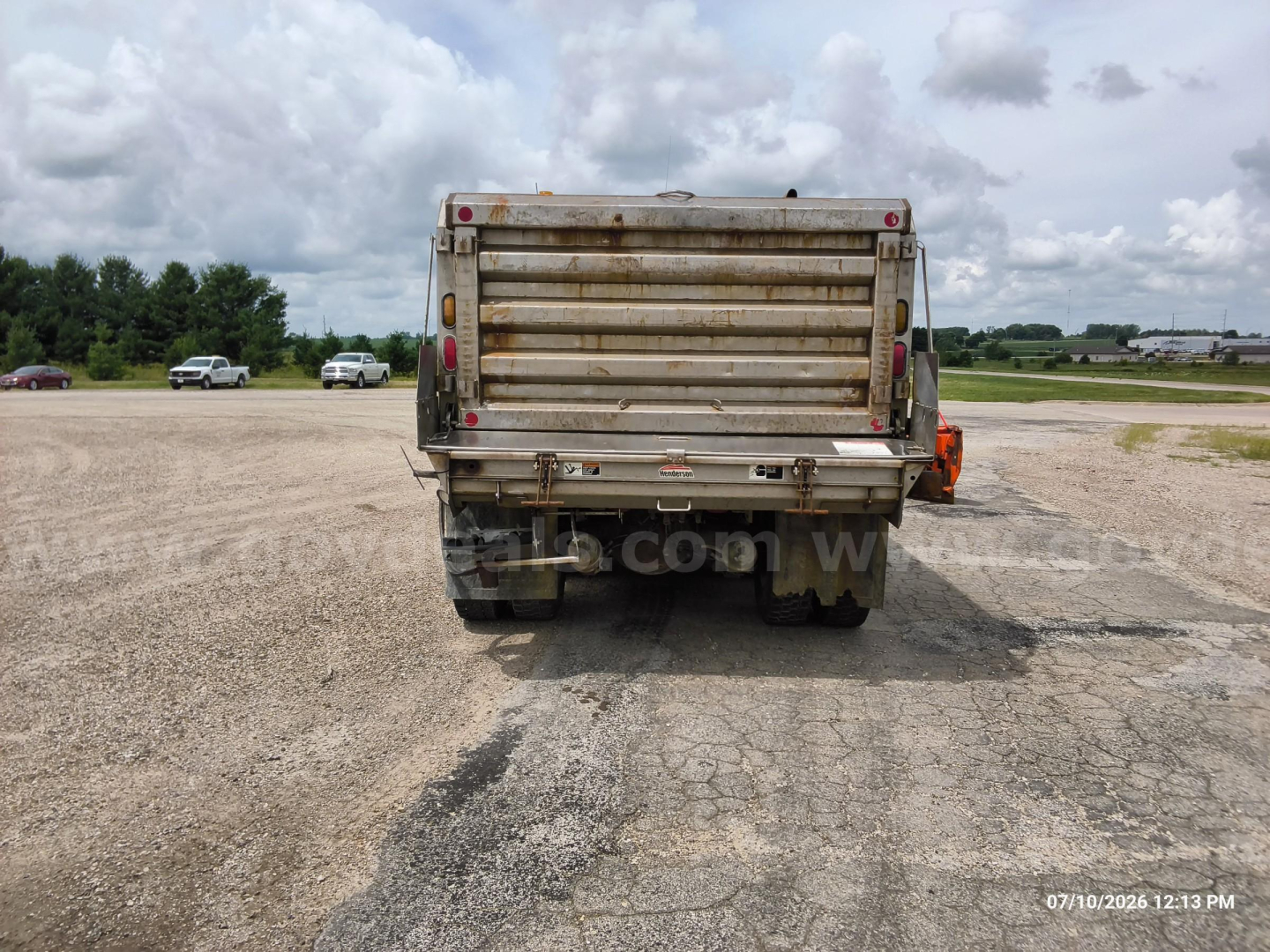 Dump truck rear view showing weathered tailgate and bumper with red reflectors and dual taillights.
