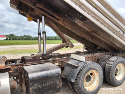 Dump truck chassis showing hydraulic lift for dump bed and dual rear axle with worn wheel rims.