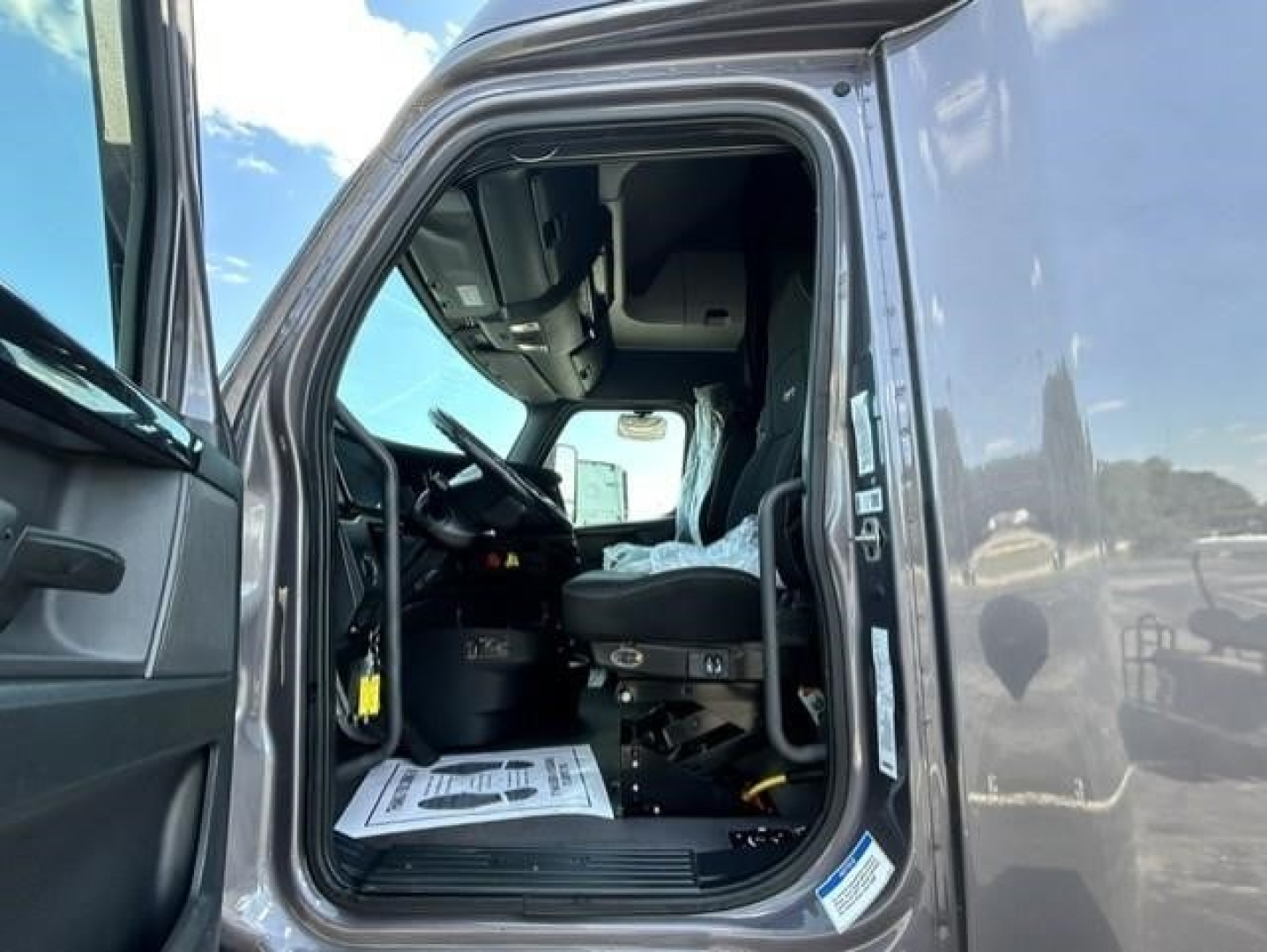 Freightliner Cascadia cab interior with driver seat and open door showing steering wheel and dashboard.