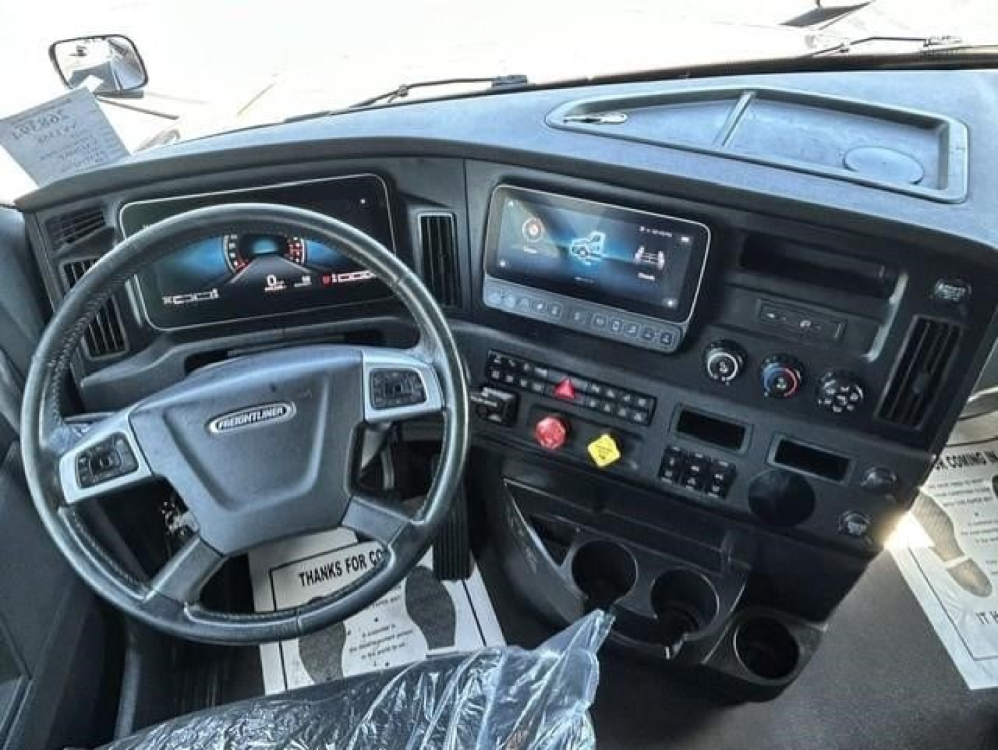 Conventional sleeper truck cab interior showing steering wheel, dashboard with digital display, center console, and control panels.
