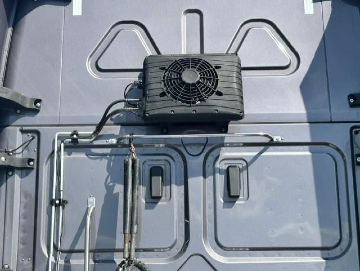 Rear of Freightliner Cascadia 126 truck door area showing a black rectangular component with a cooling fan mounted above two vertical panels and wiring harnesses.