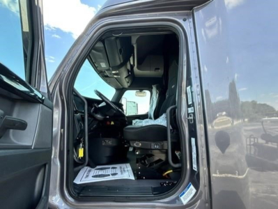 Freightliner Cascadia cab interior with driver seat and open door showing steering wheel and dashboard.