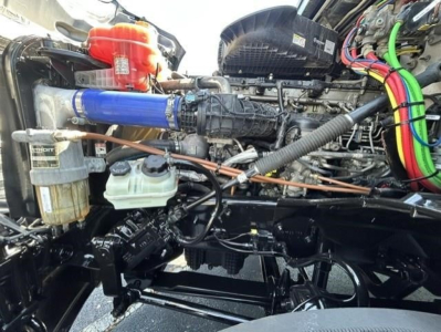 Engine bay of a Freightliner Cascadia 126 showing blue silicone hose, coolant reservoir, wiring, and various components.