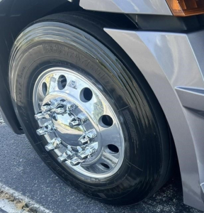 Truck wheel close-up showing chrome hub and black tire on Freightliner Cascadia 126 sleeper cab, front fender area