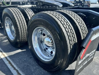 Section of a Freightliner Cascadia truck showing dual rear wheels and chrome wheel rims; treaded tires and fuel/air lines visible; mudflap with 'Se' branding, plus wheel well and frame components.