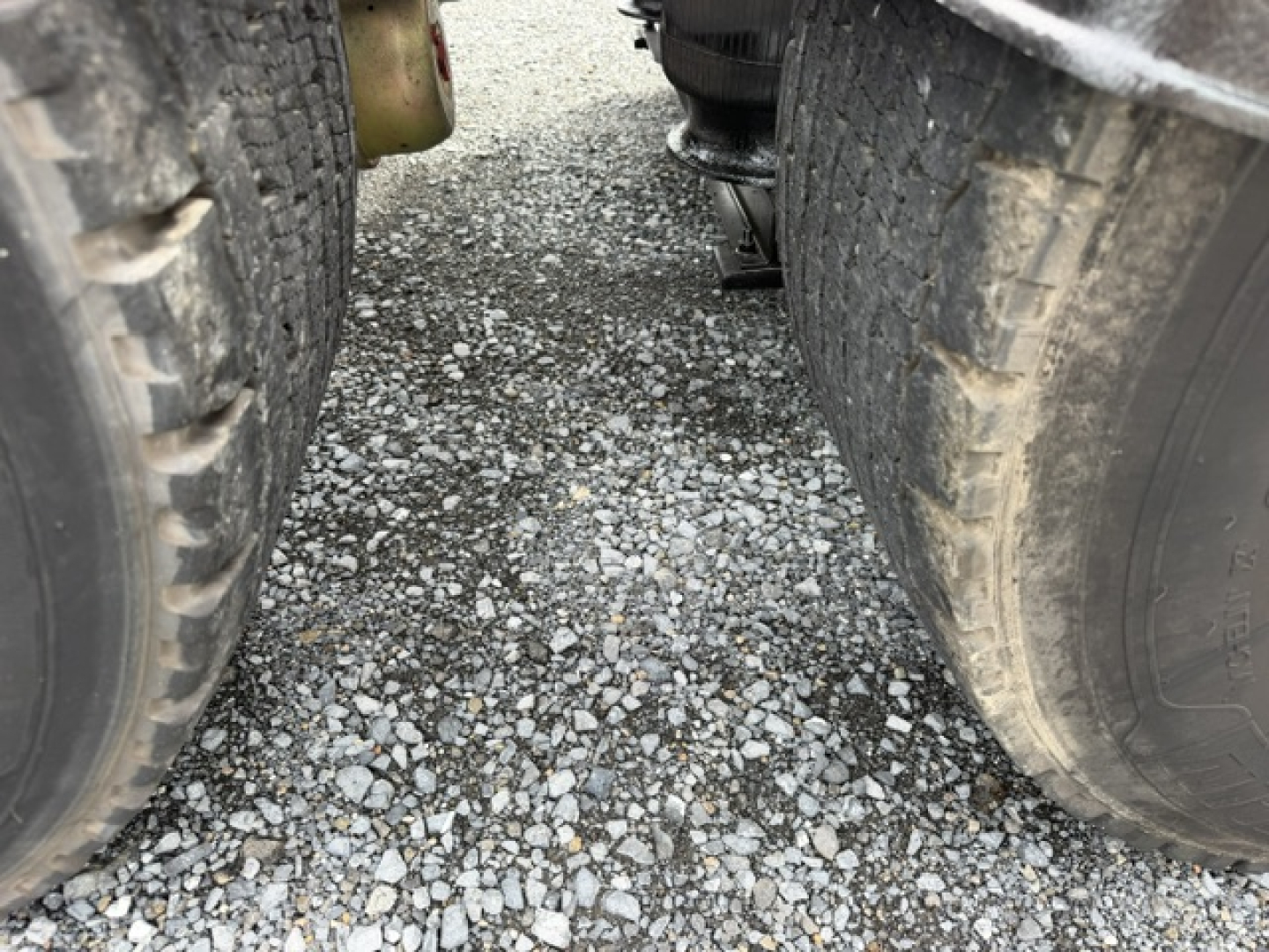 Volvo VNL64T300 tractor-trailer wheels viewed from between dual rear axles, road gravel surface in foreground.