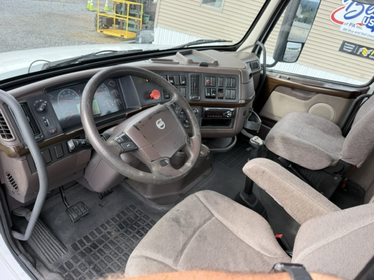 Volvo VNL64T300 cab interior showing steering wheel with Volvo emblem, dashboard gauges, center console, and two beige fabric seats.
