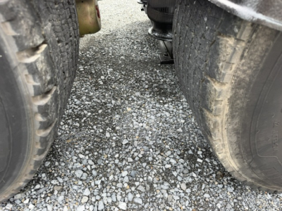  Volvo VNL64T300 tractor-trailer wheels viewed from between dual rear axles, road gravel surface in foreground.