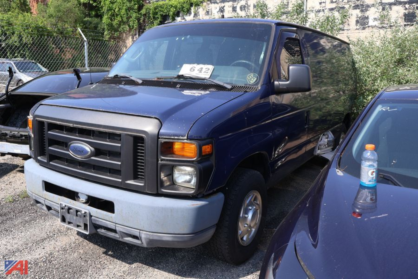 Ford E-Series van in blue, front-left view, cargo van, with black grille and gray bumper; stickered windshield and side mirror visible.