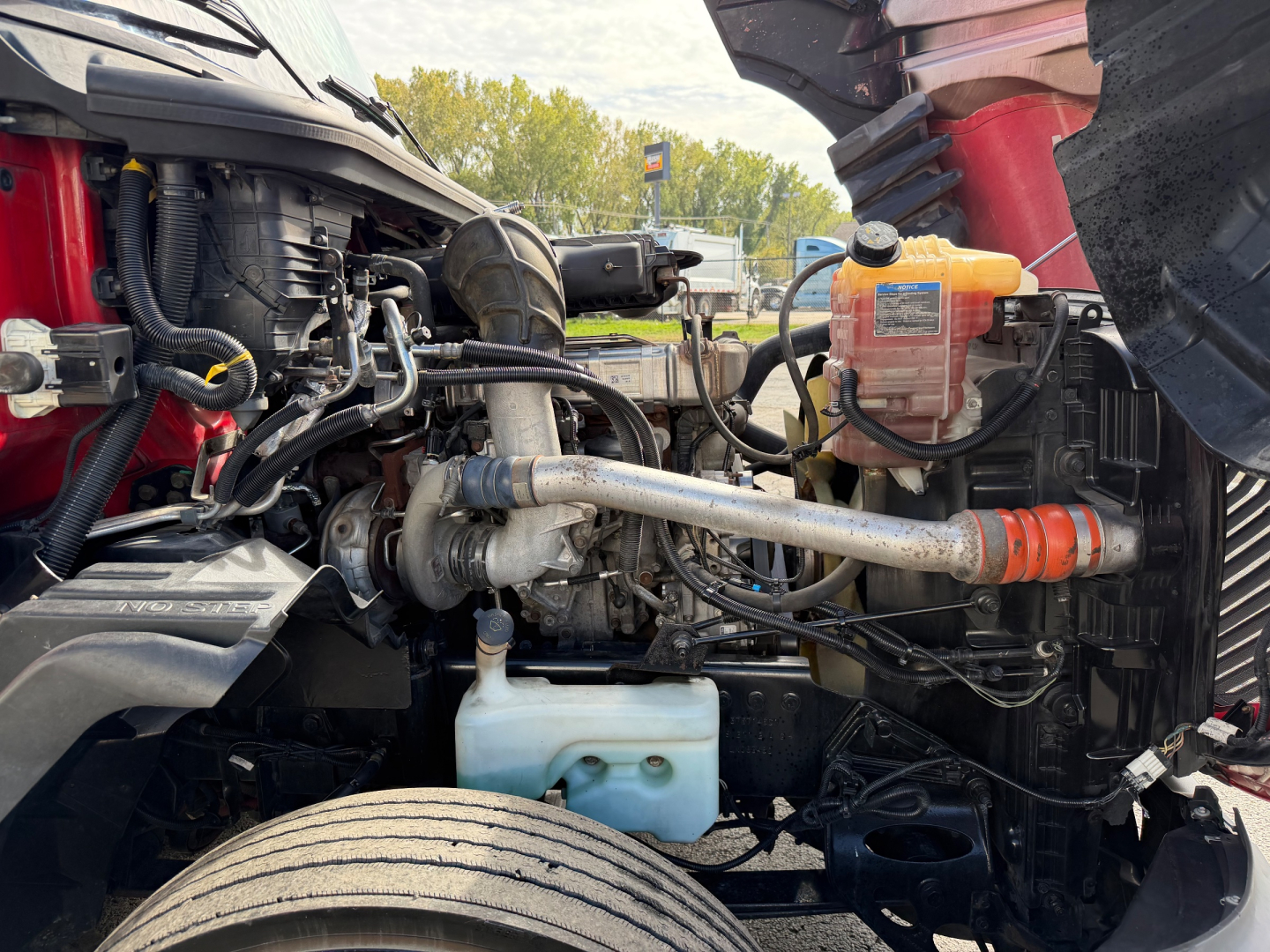 Truck engine bay showing coolant reservoir and various hoses with a translucent orange reservoir cap on the right side and blue coolant tank below; visible metal tubes and wiring.