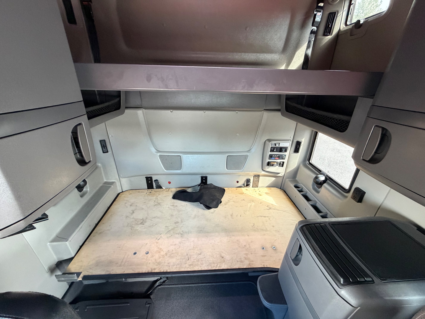 Interior sleeper cab cargo area of a 2020 International LT625 truck showing bare plywood load area, side cabinets, and overhead bunk support.