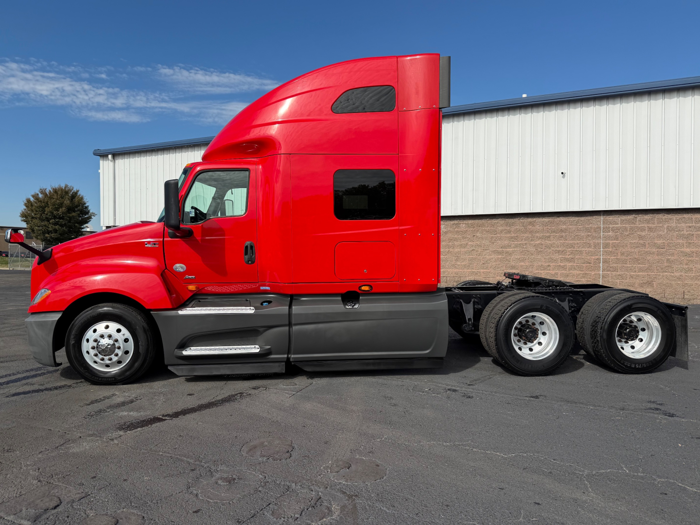 Truck side view of a red 2020 International LT625 conventional sleeper with dual rear axles and sleeper cab, parked on pavement.