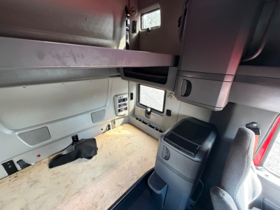 Truck cab interior showing sleeper area with overhead storage and window, Volvo International LT625? space with light wood floor and control panels.