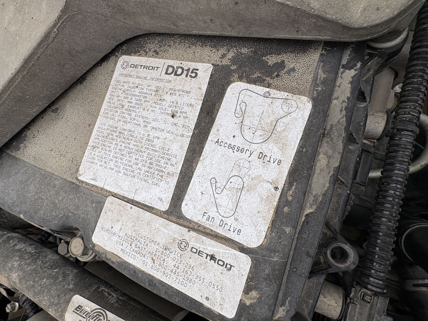 Engine bay label area showing Detroit DD15 badge with accessory drive and fan drive diagrams and a Detroit label; dirty labeling plate.