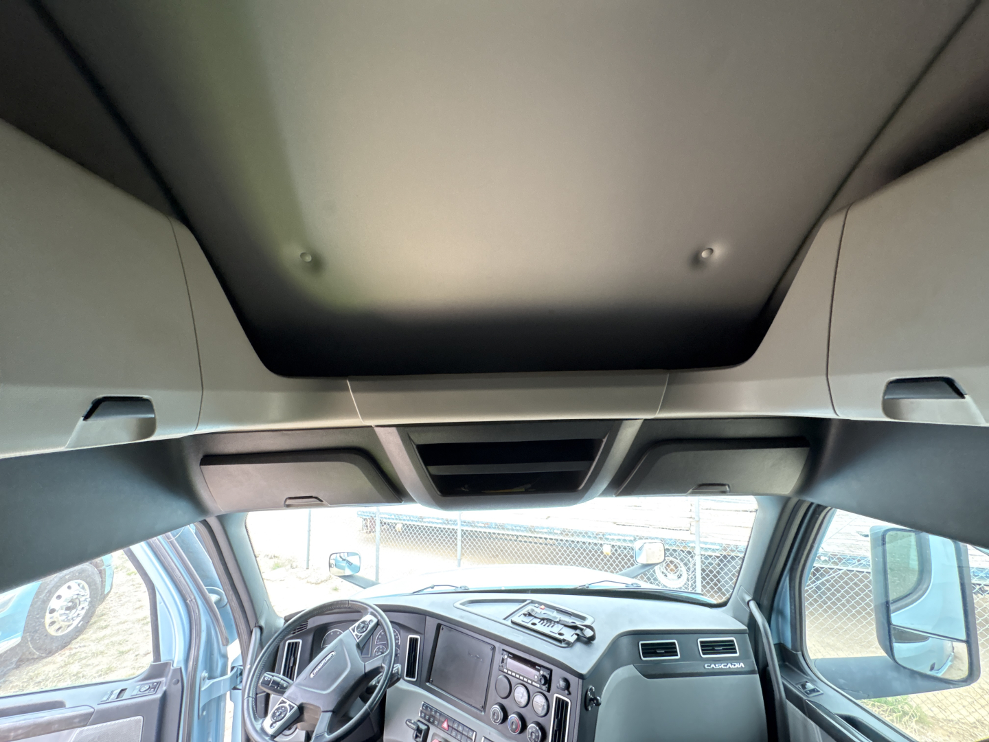 Vehicle cab interior of a Freightliner Cascadia 126 shown from the driver seat with dashboard and overhead storage visible.