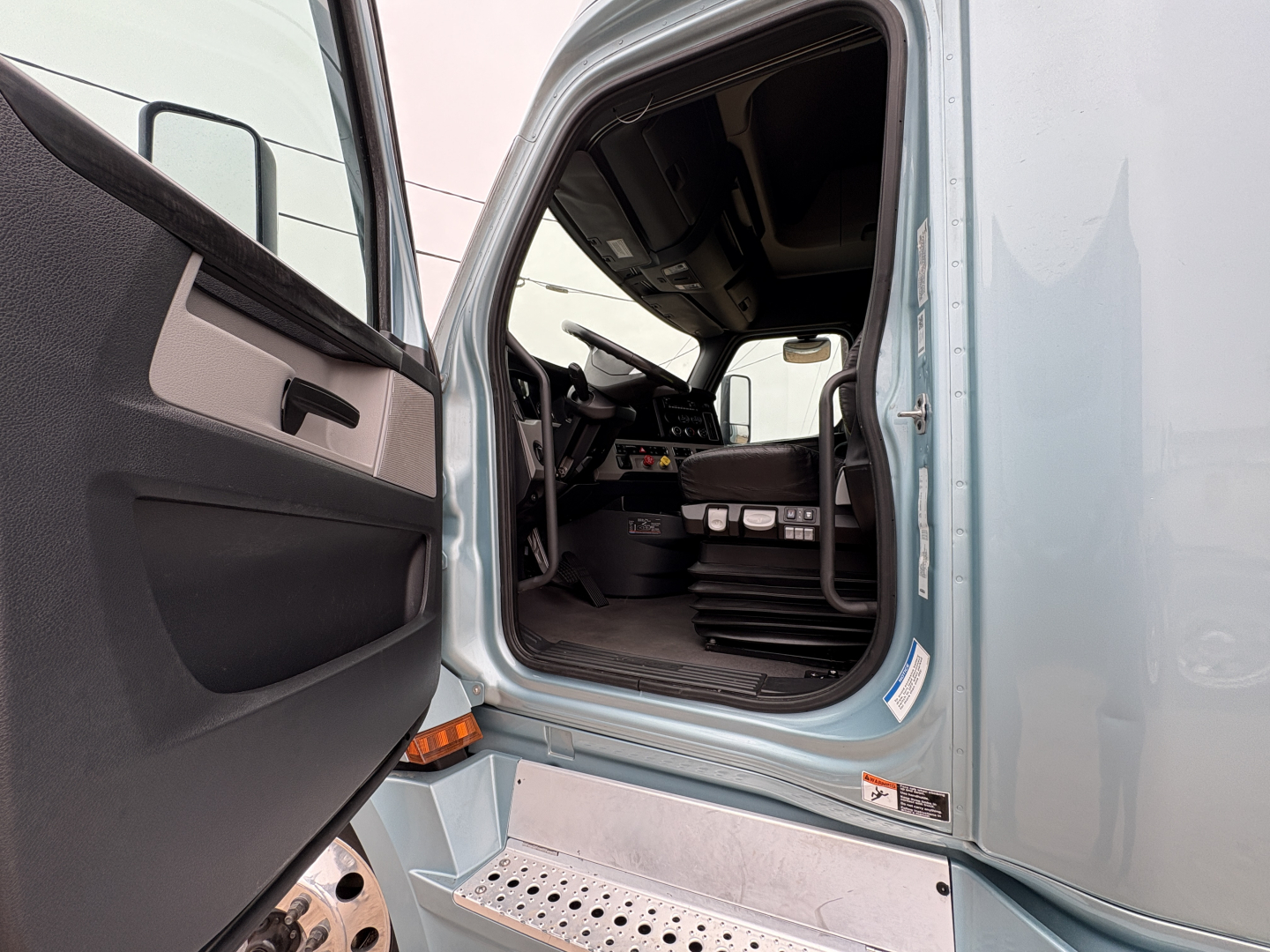 Cab interior view of a Freightliner Cascadia 126 truck with open driver door showing dashboard, steering wheel, and steps.