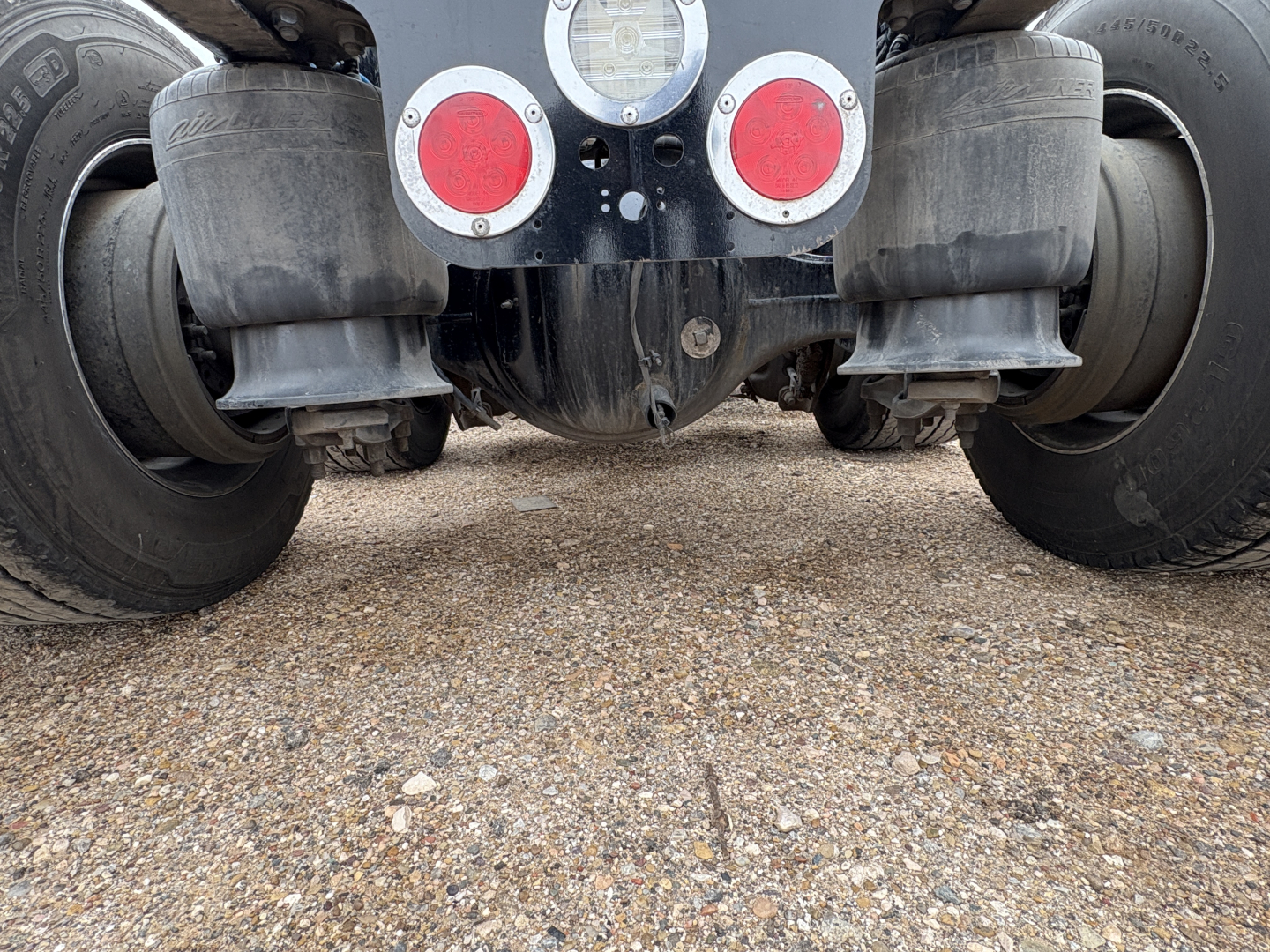 Freightliner Cascadia 126 rear view showing dual rear axles, bumper lights, and undercarriage components on gravel surface.