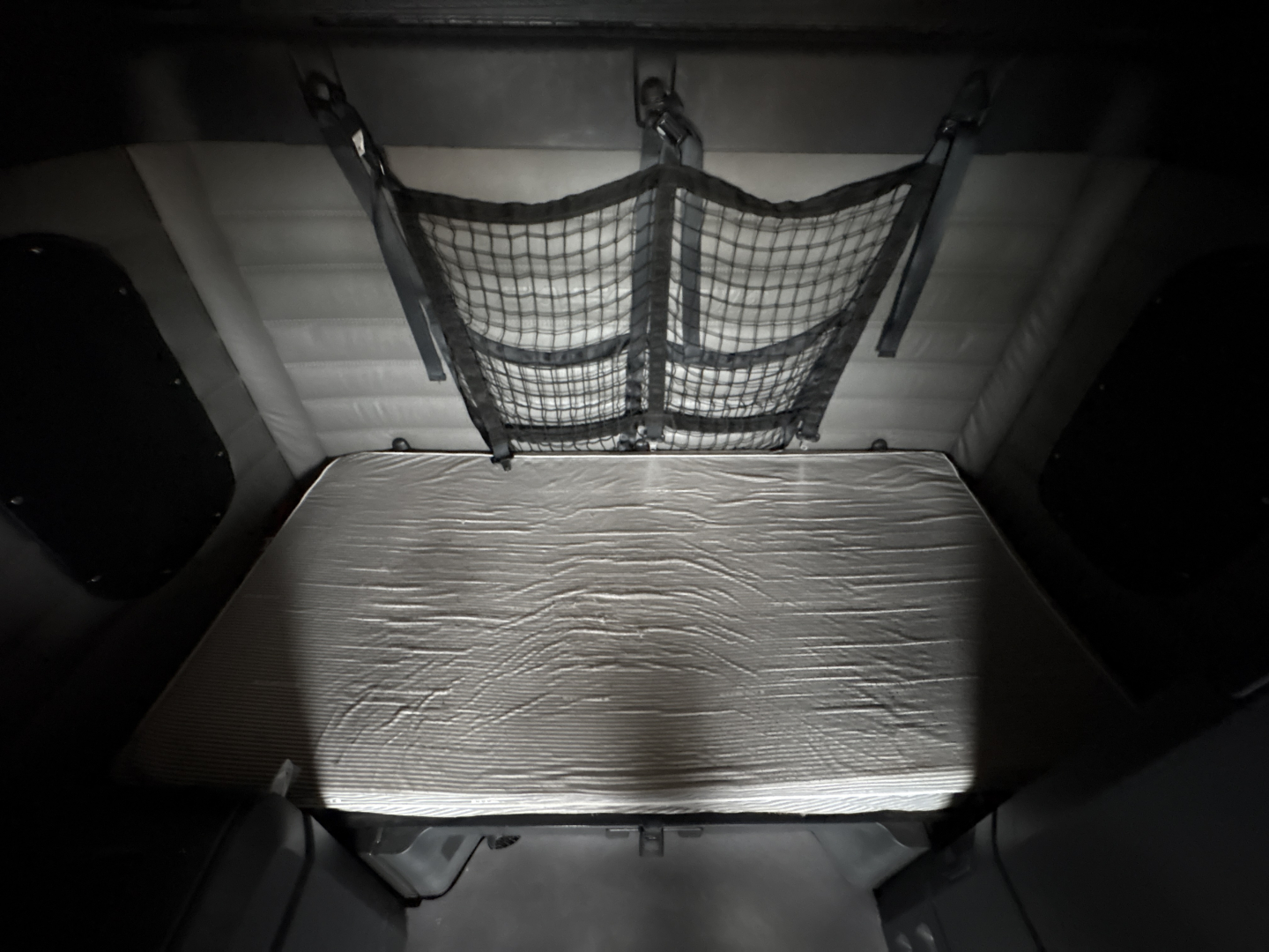 Truck sleeper cabin storage area with a netted storage pocket and a metallic insulated platform behind the sleeper.