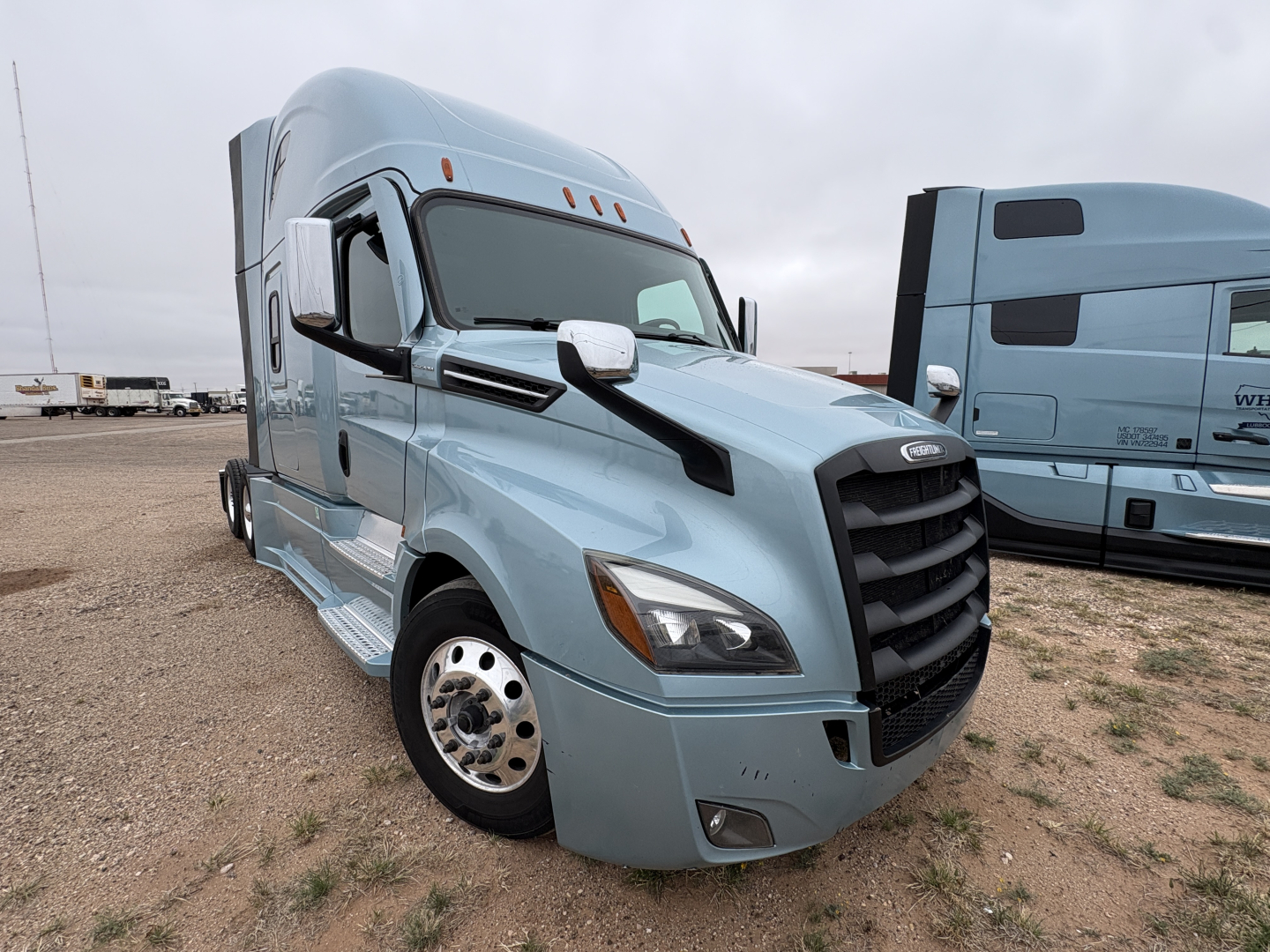 2023 Freightliner Cascadia 126 semi-truck cab in light blue, front-left view showing grille, headlight, side mirror, and wheel.
