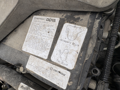 Engine bay label area showing Detroit DD15 badge with accessory drive and fan drive diagrams and a Detroit label; dirty labeling plate.