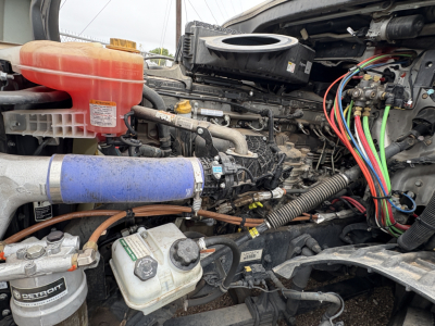 Freightliner Cascadia 126 engine bay showing coolant reservoir, blue hose, air filter, and tangled wiring harness.