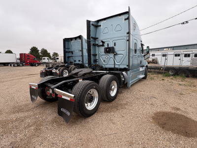 Freightliner Cascadia 126 tractor rear view showing dual rear axles and fifth-wheel, blue cab, parked in lot with other trucks.