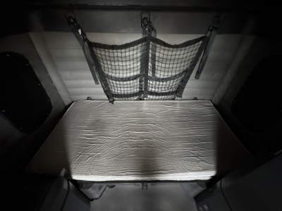 Truck sleeper cabin storage area with a netted storage pocket and a metallic insulated platform behind the sleeper.
