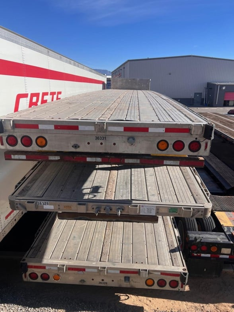 Trailer deck stacked with flatbed trailers showing rear view with lights and rust-free metal surfaces.