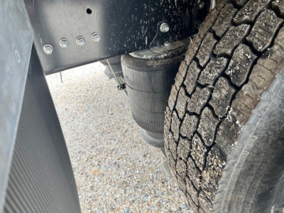 Truck rear area showing dual tandem axle with large tire treads and undercarriage components; visible is a cylindrical air reservoir or filter canister and a section of frame.