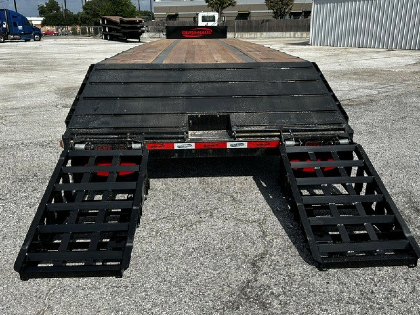 Trailer rear view showing closed tandem drop deck with dual folding ramps extended on each side.