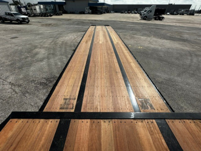 Drop deck trailer bed showing long wooden deck planks with black steel edge guides, perspective from tail ramps toward cab