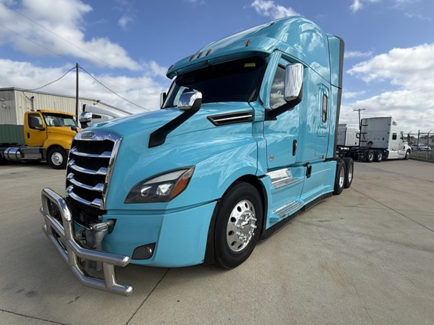 Blue Freightliner Cascadia 126 tractor-trailer cab, side view, chrome bumper guard, black grille, aerodynamic mirrors, daytime sky.
