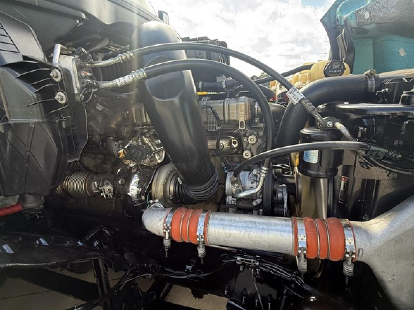 Truck engine bay close-up showing various hoses, metal pipes, and components in a Freightliner Cascadia 126 engine compartment.