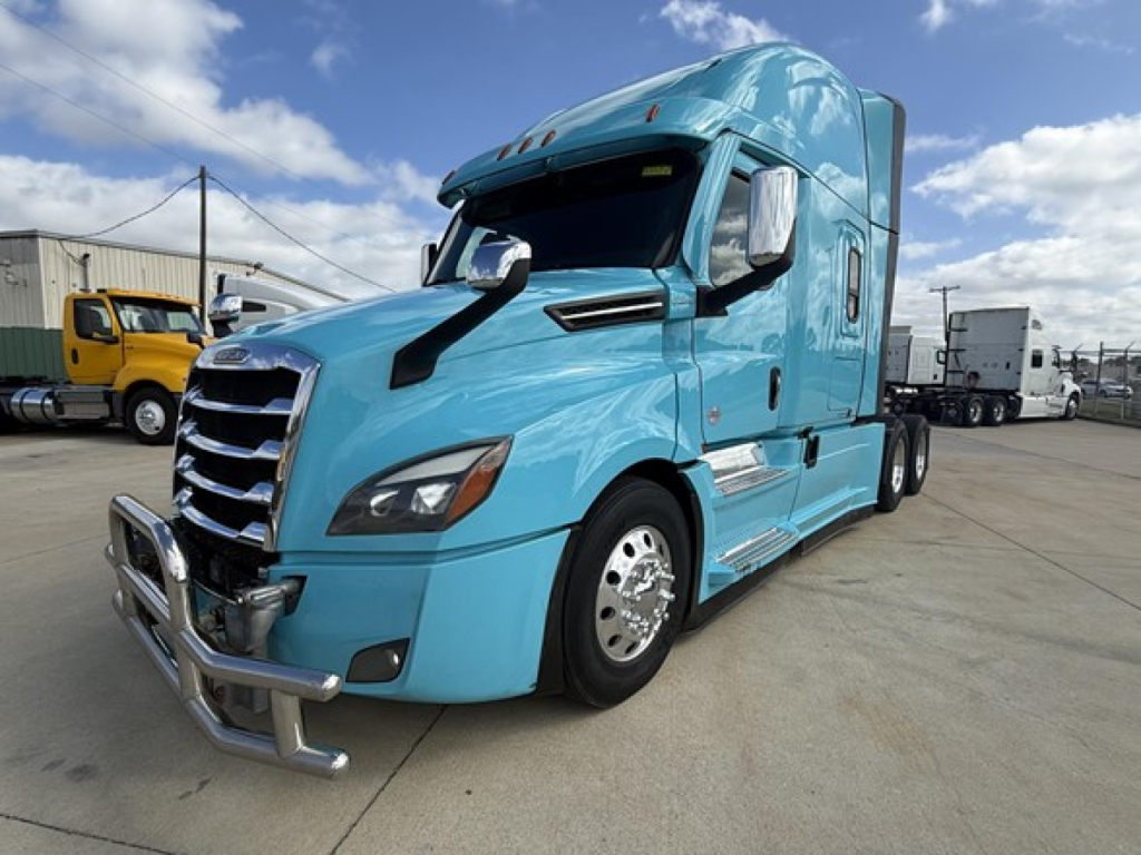 Blue Freightliner Cascadia 126 tractor-trailer cab, side view, chrome bumper guard, black grille, aerodynamic mirrors, daytime sky.